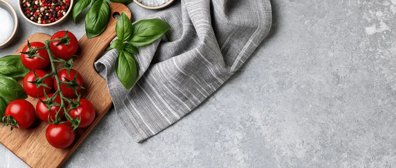 Vine tomatoes and basil on a wooden cutting board with striped cloth on gray countertop