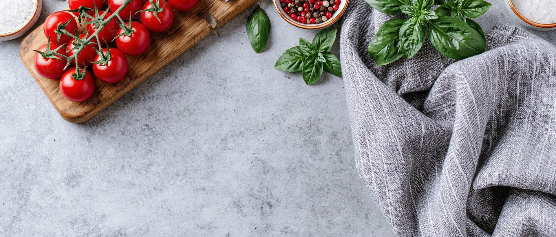 Vine cherry tomatoes on a wooden cutting board with basil and spices on a gray countertop