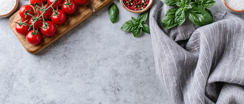 Vine cherry tomatoes on a wooden cutting board with basil and spices on a gray countertop
