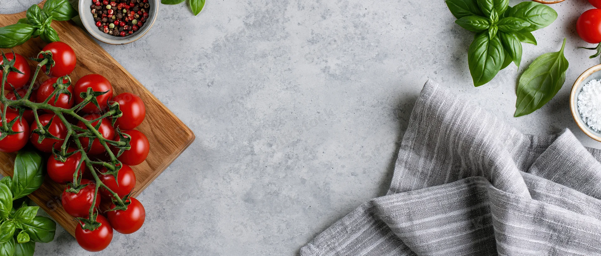 Vine cherry tomatoes with basil and spices on a wooden board and gray countertop, flat lay food styling