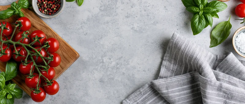 Vine cherry tomatoes with basil and spices on a wooden board and gray countertop, flat lay food styling