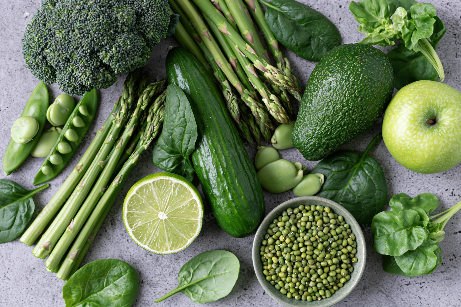 Assorted green vegetables and fruits arranged in a flat lay on a gray countertop