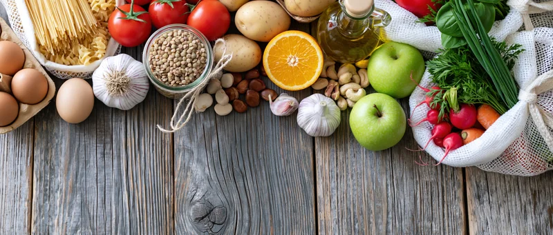 Assorted fresh groceries arranged on a rustic wooden table in a flat lay composition