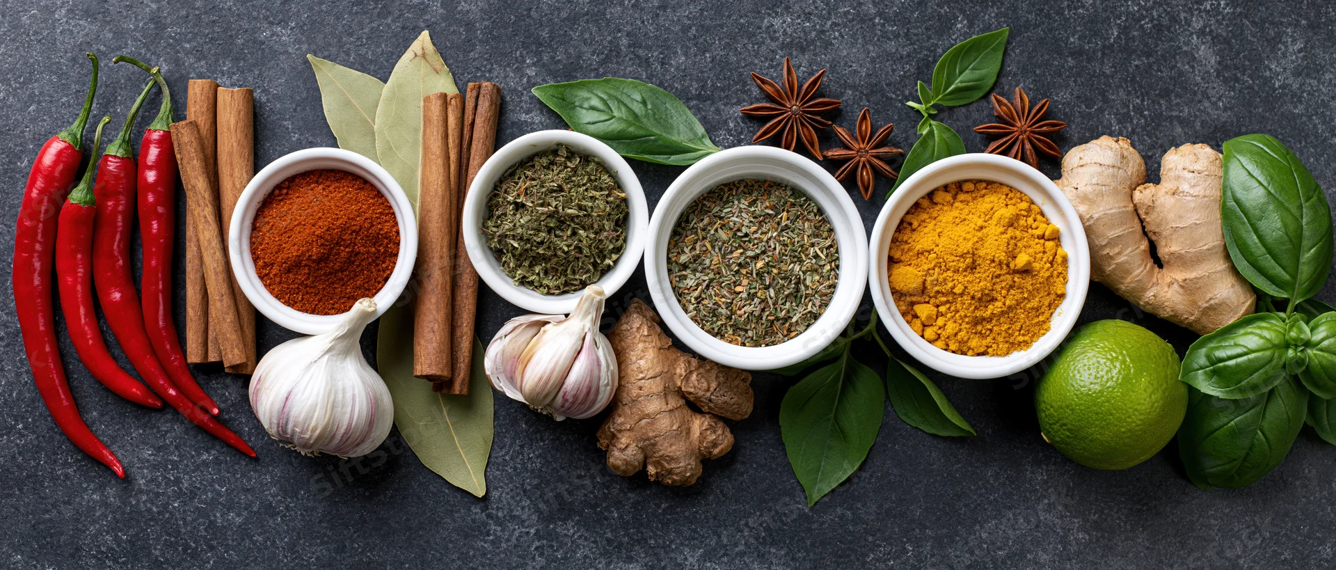 Assorted spices and fresh herbs arranged in a flat lay on dark surface