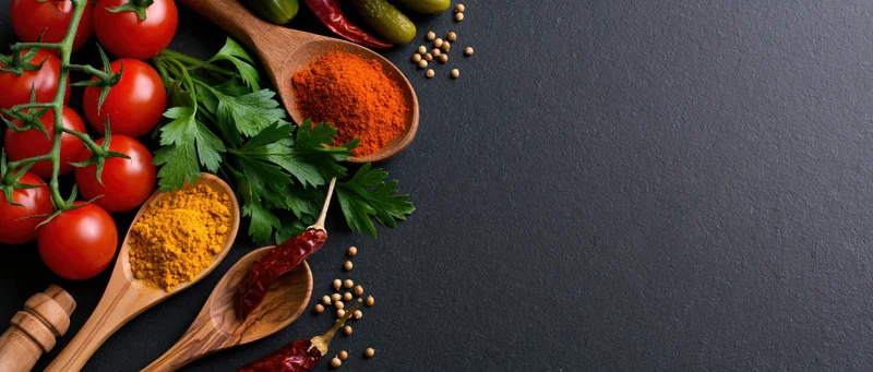 Cherry tomatoes on vine with wooden spoons holding spices and herbs arranged on dark surface