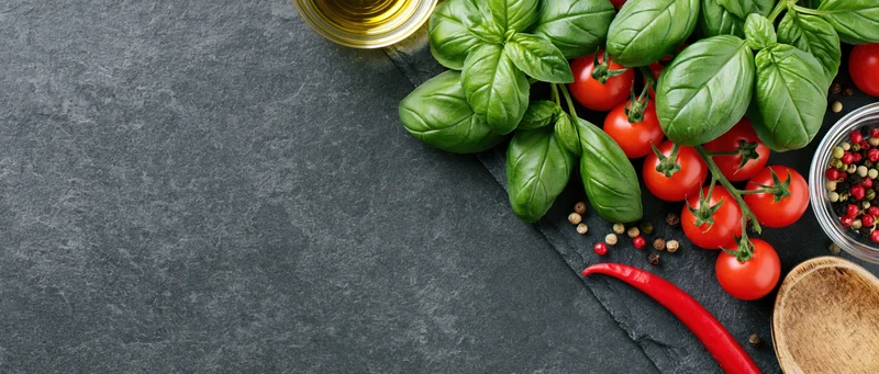 Fresh basil and cherry tomatoes on vine arranged with spices and oil on dark slate surface