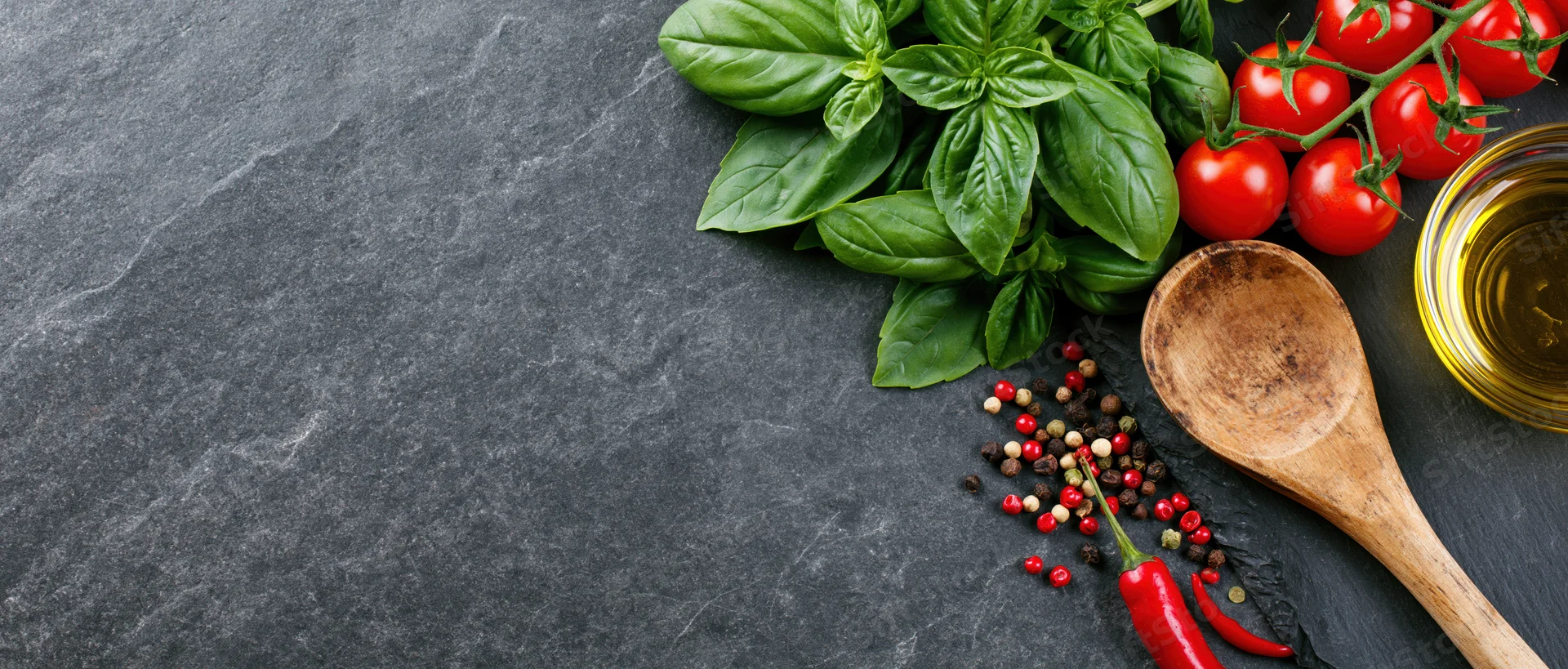 Fresh basil and cherry tomatoes on vine with wooden spoon and olive oil on dark slate countertop