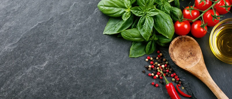Fresh basil and cherry tomatoes on vine with wooden spoon and olive oil on dark slate countertop
