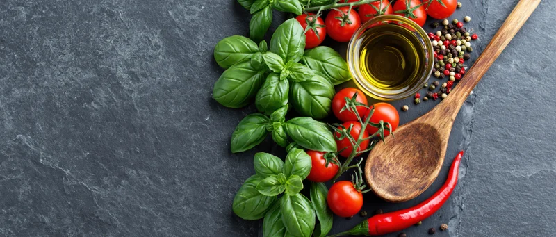 Fresh basil and cherry tomatoes on vine with olive oil and spices arranged on slate surface