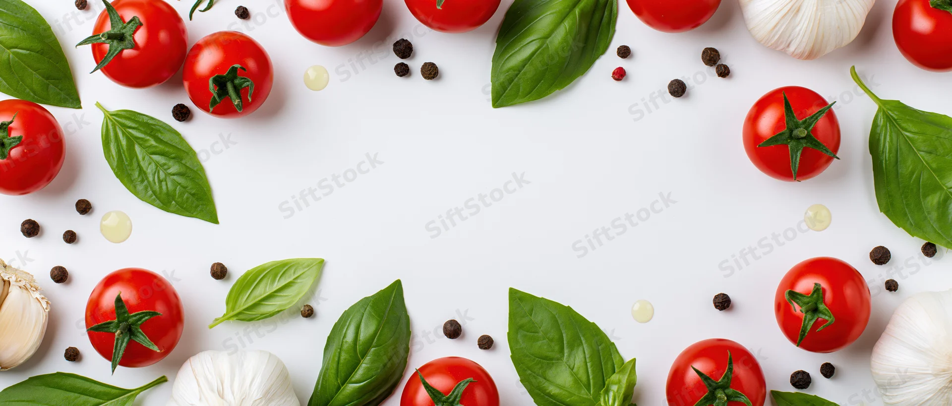 Cherry tomatoes, basil leaves, garlic bulbs, and peppercorns arranged in a border on white surface with central copyspace