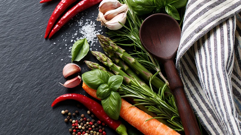 Fresh vegetables and herbs arranged with a wooden spoon on a dark slate surface
