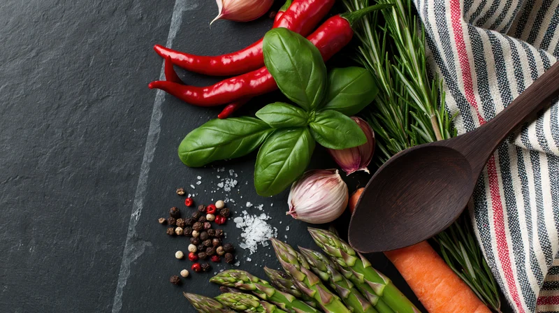 Fresh cooking ingredients and a dark wooden spoon arranged on a slate surface with a striped cloth