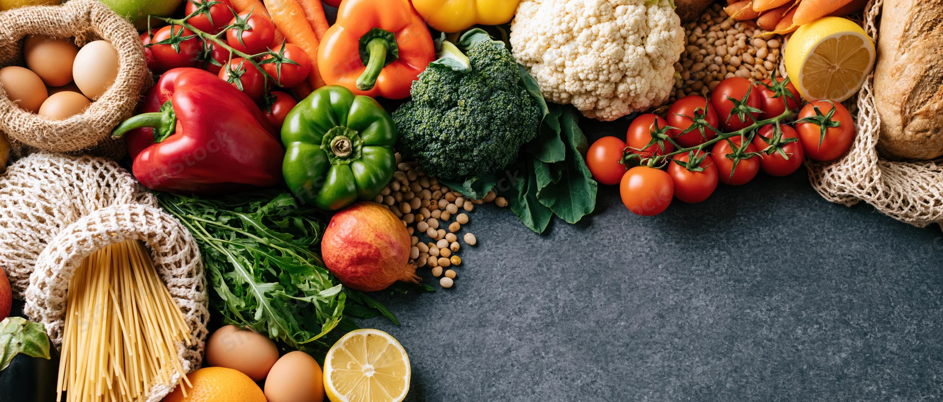 Fresh groceries arranged in a flat lay on dark grey concrete surface with copyspace