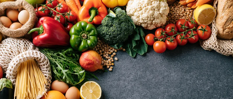 Fresh groceries arranged in a flat lay on dark grey concrete surface with copyspace