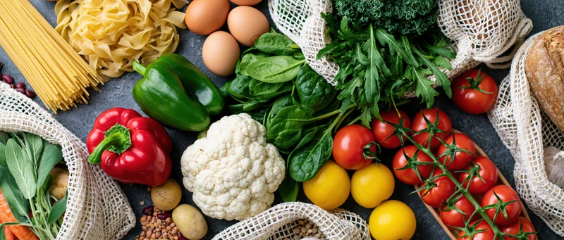 Fresh vegetables and pantry staples arranged in net bags on dark surface