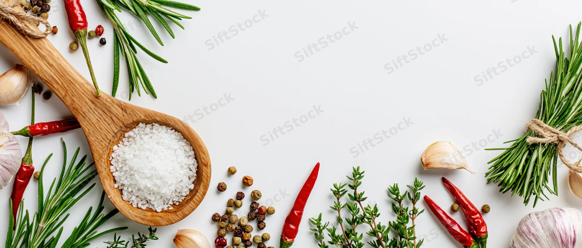 Fresh herbs and spices arranged around edges on white surface with copyspace