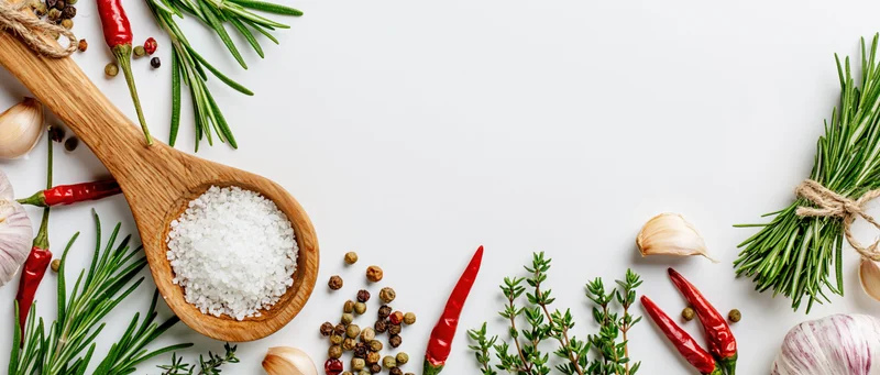 Fresh herbs and spices arranged around edges on white surface with copyspace