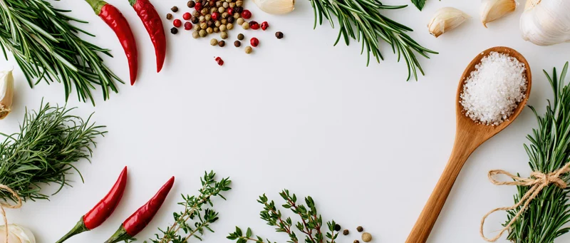 Fresh herbs and spices arranged around edges on white surface with central copyspace