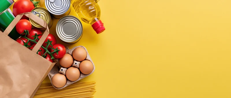 Grocery staples arranged on a bright yellow surface with copyspace