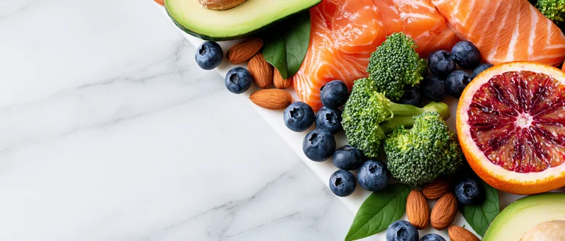 Healthy foods arranged along the right edge of a marble surface with copyspace on the left