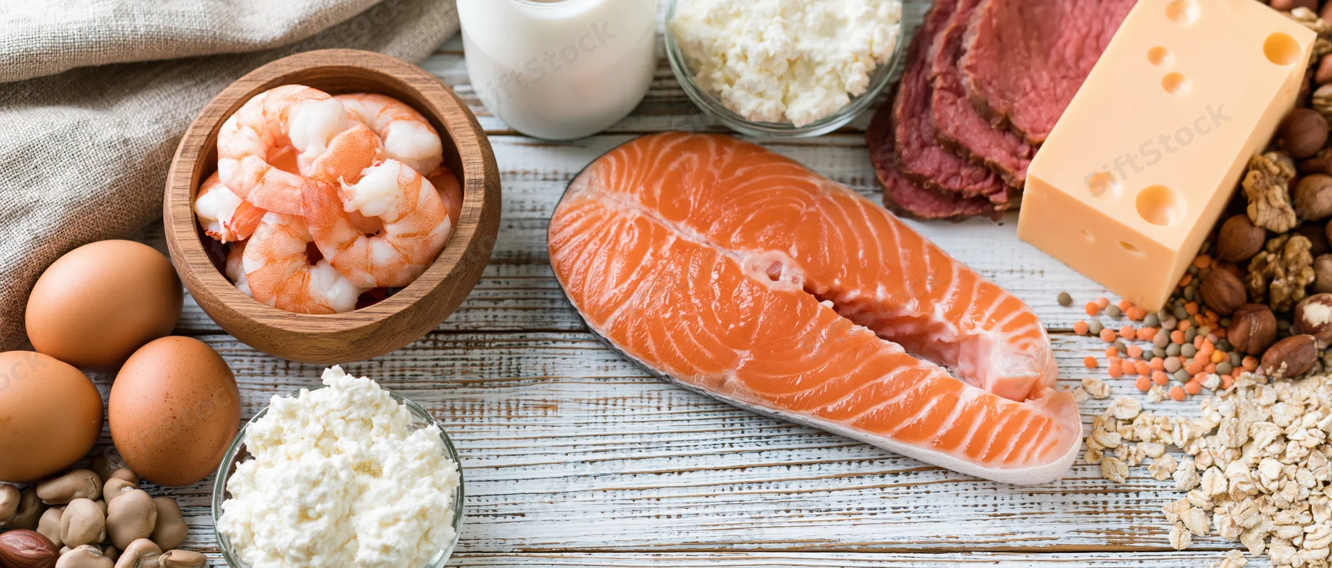 High-protein foods arranged on a white-painted wooden table in a flat lay composition