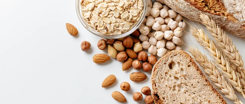 Flat lay of oats, nuts, chickpeas, bread and wheat stalks on white surface
