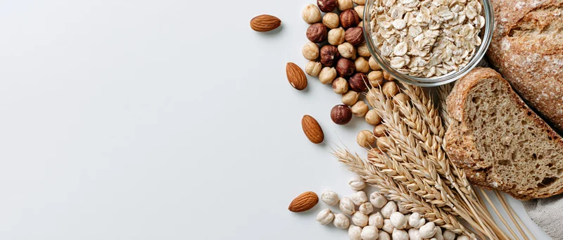 Flat lay of oats, nuts, bread, and wheat stalks arranged on white surface with copyspace
