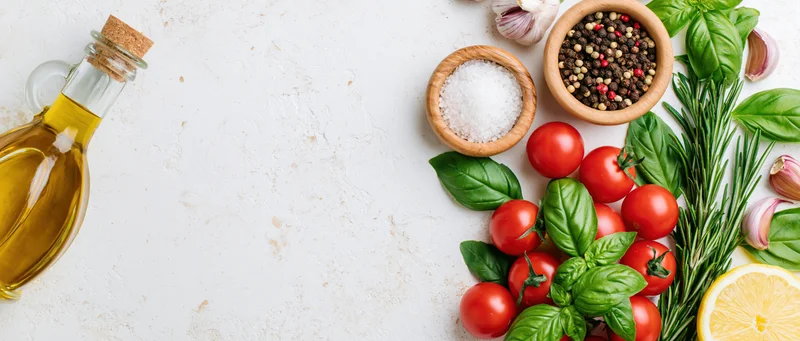 Fresh vegetables and herbs with olive oil and spices arranged on white surface