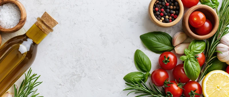Fresh herbs and vegetables arranged with olive oil and salt on a white countertop for cooking