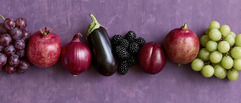 Purple and red fruits and vegetables arranged in a row on a textured purple surface
