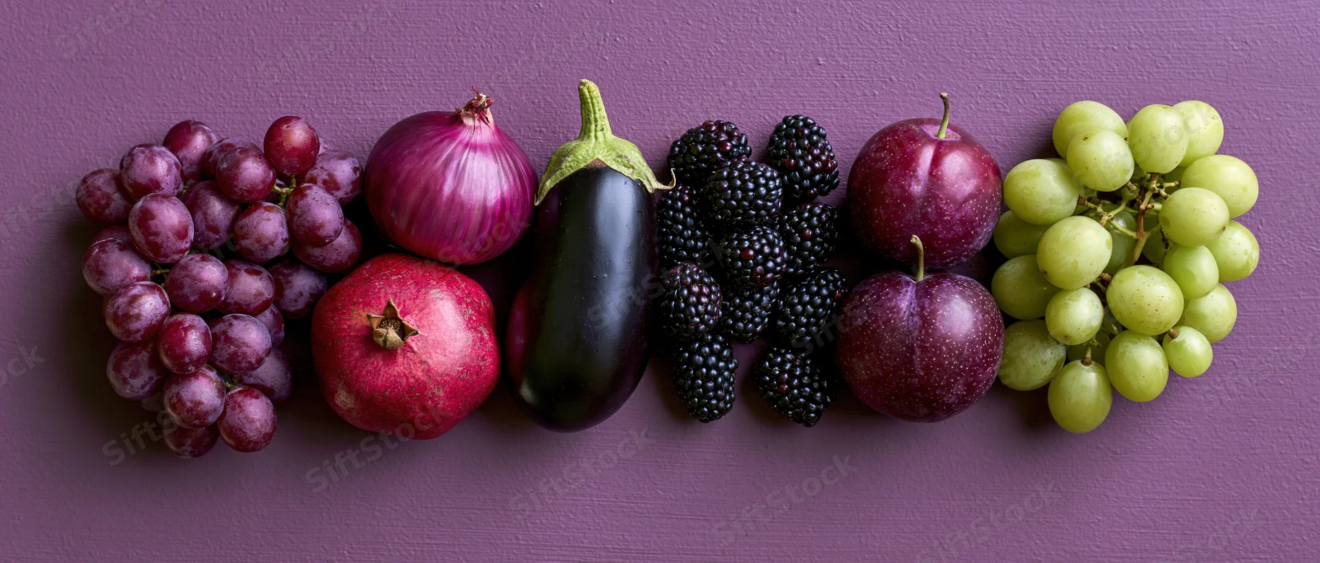 Purple and red fruits and vegetables arranged in a row on a textured surface
