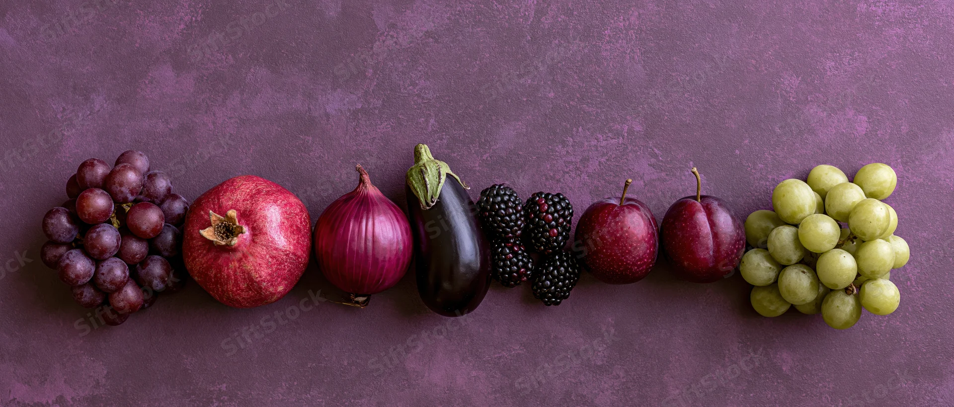 Purple and red fruits and vegetables arranged in a row on a textured surface