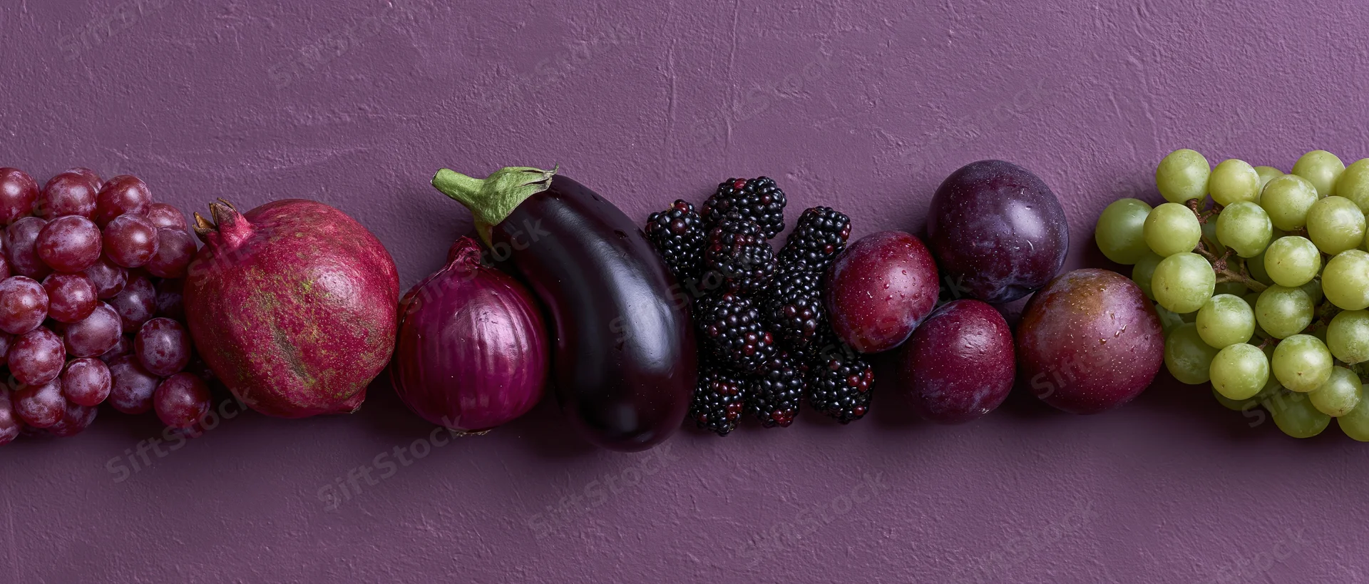 Purple and red fruits and vegetables arranged in a row on a textured surface