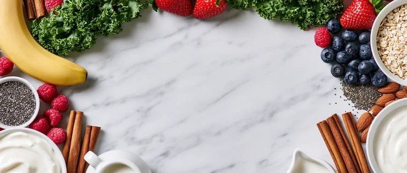 Breakfast ingredients arranged in a circular frame on a marble countertop with copyspace in center
