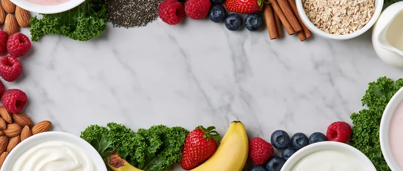Smoothie and breakfast ingredients arranged in a border on a marble surface with copyspace in center