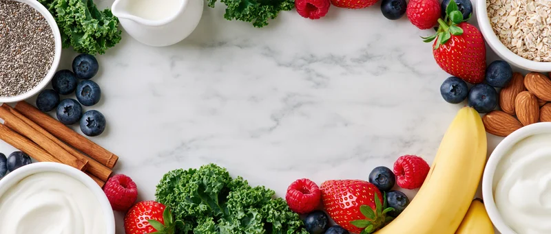 Smoothie and breakfast ingredients arranged in a circle on marble surface with central copyspace