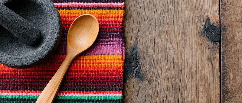 Wooden spoon and stone mortar on colorful striped textile beside rustic wooden surface