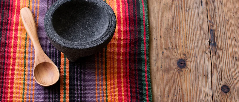 Wooden spoon and stone mortar on colorful striped rug beside rustic wooden table