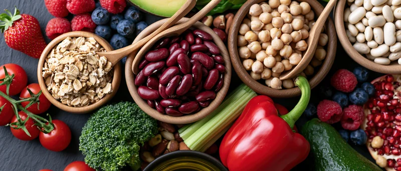 Assorted healthy foods including vegetables, fruits, beans and grains arranged in wooden bowls on slate surface
