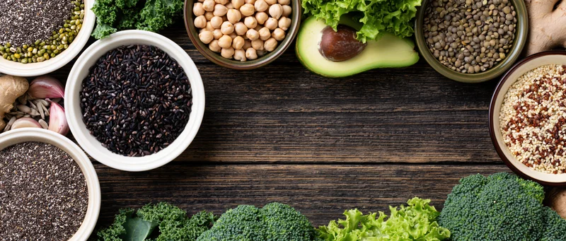 Assorted superfoods and legumes arranged in bowls and piles on a dark wooden table with copyspace in center