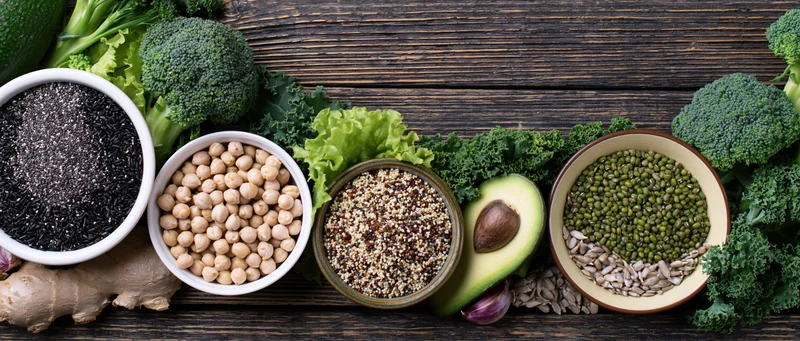 Assorted superfoods and legumes arranged in bowls on a dark wooden surface with leafy greens and herbs