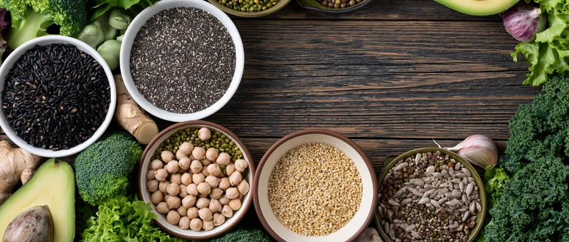 Assorted superfoods and legumes arranged in bowls on a dark wooden surface with copyspace in center