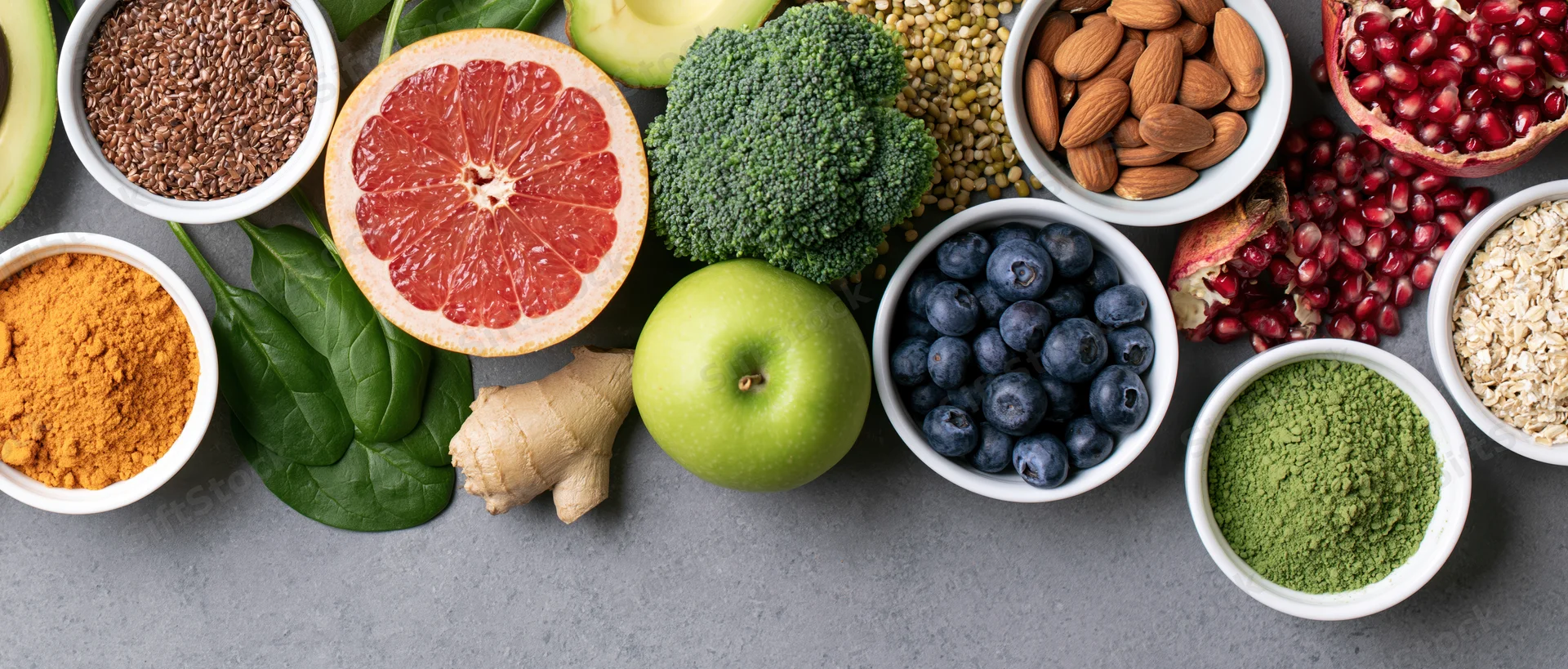 Assorted whole foods arranged in bowls and clusters on a gray surface in an overhead flat lay composition