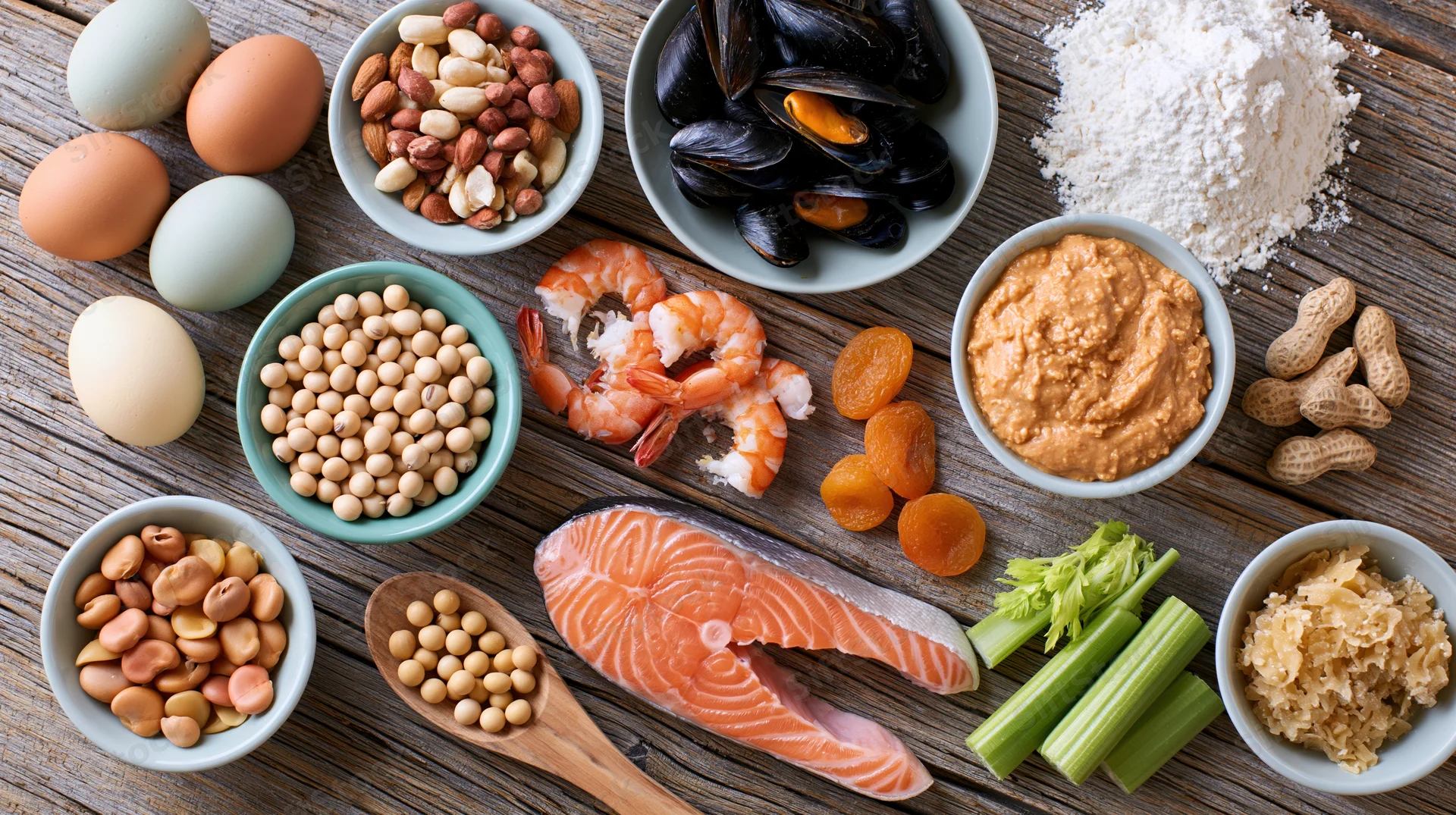 Various common food allergens arranged in bowls and on a wooden table in an overhead flat lay composition