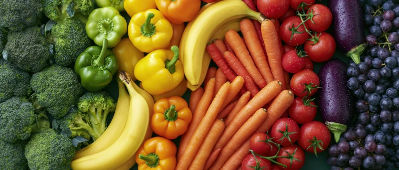 Overhead flat lay of fresh fruits and vegetables arranged in a colorful rainbow pattern