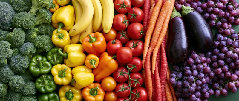 Overhead flat lay of fresh fruits and vegetables arranged in colorful rows on a green surface