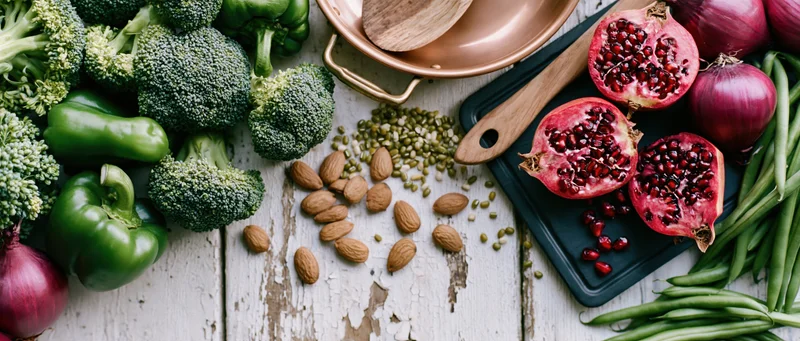 Fresh vegetables and fruits arranged with nuts and lentils on a white wooden surface in a flat lay overhead composition