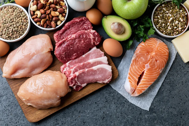 Raw proteins and whole foods arranged on a dark countertop in a flat lay overhead composition