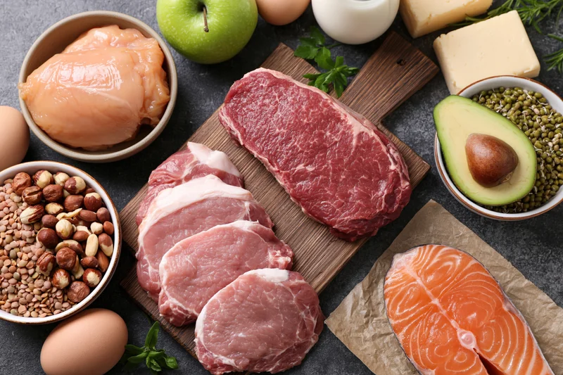Raw proteins and whole foods arranged on dark stone surface in flat lay overhead view