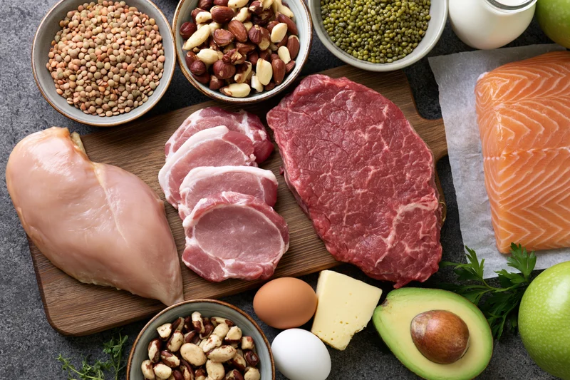 Raw proteins and whole foods arranged on a dark surface in a flat lay overhead composition